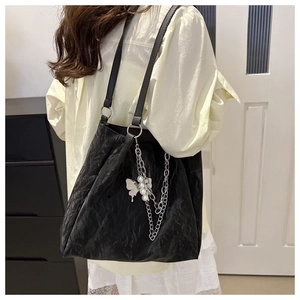 Close-up of black pleated tote bag featuring a decorative butterfly and pearl metal chain