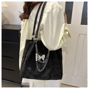 Close-up of black wrinkled tote bag with silver chains, white pearls, and butterfly charms