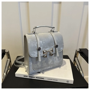 Détail d'un sac à main gris argenté avec nœud métallique et boucle sur des livres blancs