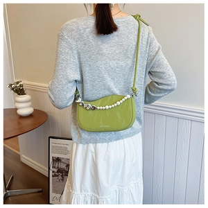 Detail of green half-moon bag with large pearl and silver heart chain strap on model