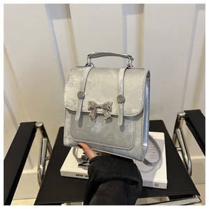 Détail d'un sac à main argenté métallisé avec nœud décoratif et bandoulière réglable