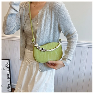Close-up of green crescent bag with pearl heart chain and leather strap details