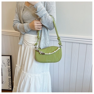 Close-up of green nylon crescent bag featuring pearl chain and heart charm detail