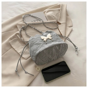 Détail d'un sac seau plissé argenté avec ornement de nœud sur un blazer beige