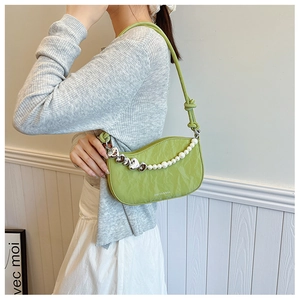 Close-up of avocado green PU leather bag with pearl and heart chain on model shoulder