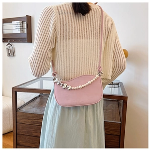 Detail of light pink crescent bag featuring pearl and silver heart chain on the shoulder
