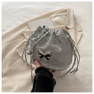 Détail du sac seau plissé argenté avec ornement papillon métallique et bandoulière chaîne