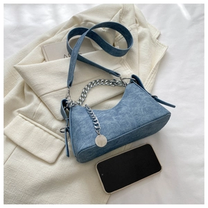 Close-up of blue textured crescent bag with silver chain strap on white blazer