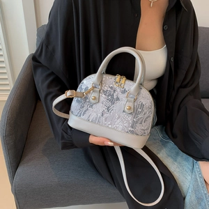 Detail view of light gray shell bag with white embroidery and golden zippers