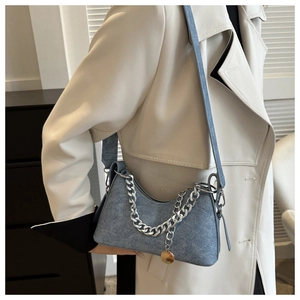 Detail of blue denim crescent bag with chunky silver chain and gold charm on model