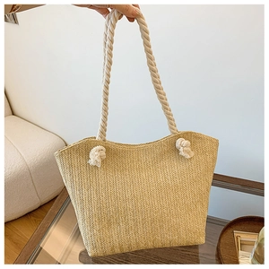 Detail view of woven straw tote bag featuring thick white cotton rope handles and knots