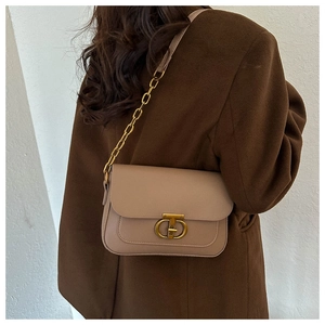 Détail d'un sac à bandoulière en cuir beige avec chaîne dorée porté sur un manteau brun