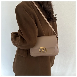 Sac sous le bras beige avec fermoir doré porté par un mannequin en manteau d'hiver