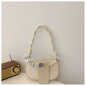 Detail of cream half-moon bag with woven strap and pearl heart charm next to a phone