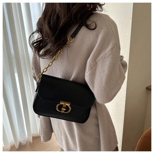 Sac sous le bras en cuir noir chic avec fermoir doré porté à l'épaule par un mannequin