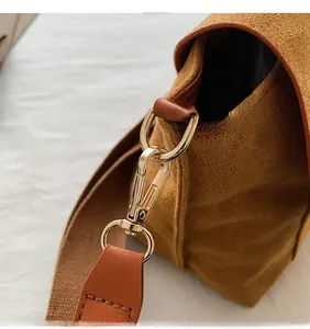 Détail de la quincaillerie dorée et texture daim sur un sac à bandoulière marron