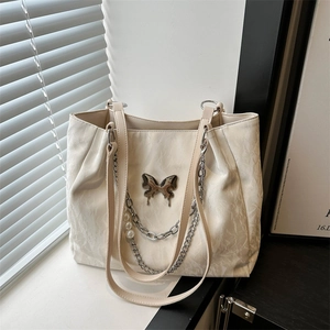 Minimalist beige tote bag with butterfly ornament and pearl chain details in a sunny interior