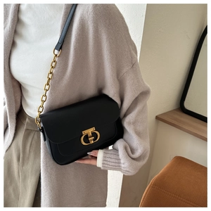 Détail du petit sac noir avec fermoir TD doré et bandoulière en chaîne porté par un mannequin