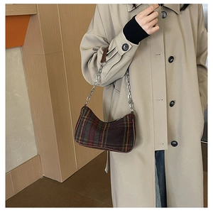 Detail of plaid baguette bag with silver chain strap on a khaki trench coat