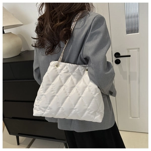 Détail d'un sac matelassé blanc avec chaîne dorée porté à l'épaule pour femme
