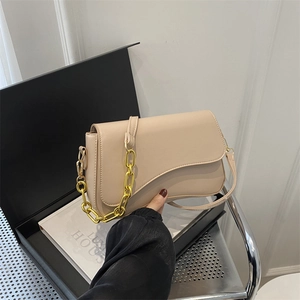 Minimalist beige crossbody bag with gold chain strap shown against luxury gift box background