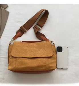 Détail du sac bandoulière en daim jaune avec large sangle tressée marron et téléphone témoin