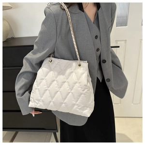 Detail view of a white quilted tote bag with a golden chain strap in a modern setting
