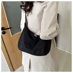 Close-up of black waterproof nylon crescent bag styled with a beige trench coat