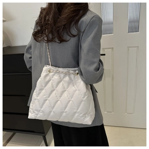 Détail d'un sac seau blanc matelassé avec bandoulière en chaîne porté à l'épaule