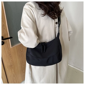 Detail of black nylon crescent crossbody bag worn by a model in a minimalist room