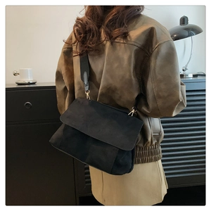 Gros plan du sac bandoulière en daim noir avec large sangle et boucle dorée ajustable