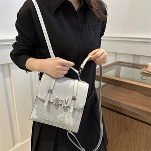 Sac bandoulière chic gris métallisé avec nœud pour femme porté sur une robe noire