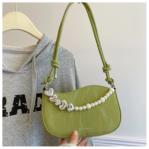 Detail view of green pleated shoulder bag featuring heart charms and pearl chain