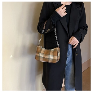 Close-up of a plaid hobo bag with silver chain strap worn by a model in a black coat