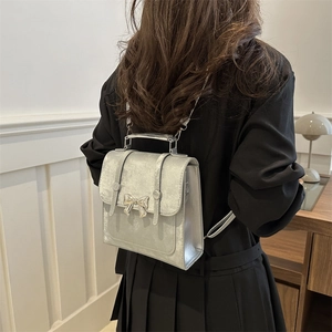 Sac à dos argenté métallisé avec nœud porté par un mannequin dans un décor moderne