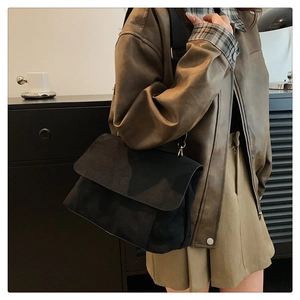 Détail d'un sac à bandoulière noir mat avec rabat et texture douce en daim synthétique
