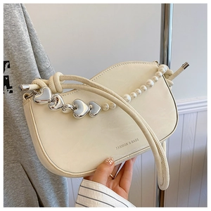 Detail of cream half-moon bag featuring pearl chain and silver heart charm decoration