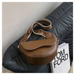 Close-up of brown matte leather saddle bag with wide woven strap on a black sofa