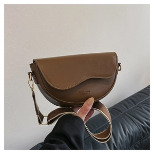 Close-up of brown saddle bag with adjustable wide canvas strap and brand lettering