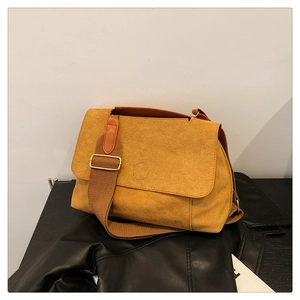 Détail du sac bandoulière en daim jaune avec large sangle en toile sur fond épuré