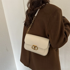 Sac bandoulière chic en cuir crème avec détails dorés porté par un mannequin