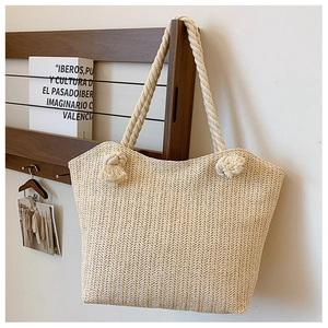 Detail of hand-woven straw tote with cotton rope handles and tassel knots on wooden shelf
