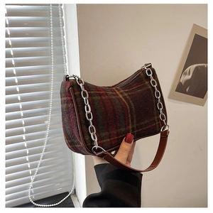 Close-up of red and green plaid baguette bag with brown leather strap and silver chain