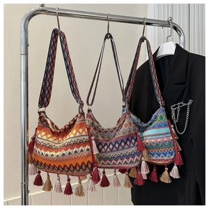 Three bohemian knit crossbody bags with colorful geometric patterns and long fringe details