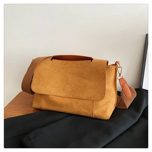 Détail d'un sac bandoulière en daim jaune gingembre avec rabat embossé et sangle large