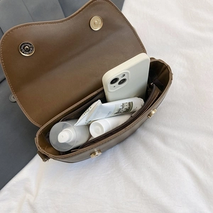 Brown leather saddle bag showing open interior storage and gold metallic clasp closure