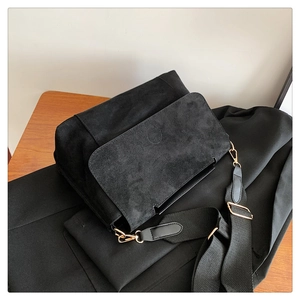 Détail du sac bandoulière en daim noir avec sangle large et boucles en métal doré