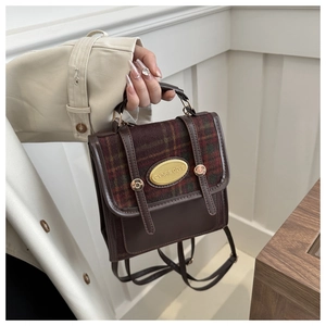 Detail of vintage mini backpack showing brown leather and plaid fabric with gold emblem