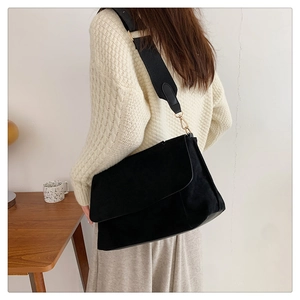 Détail du sac bandoulière en daim noir avec large sangle porté par un modèle