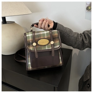 Detail of British style plaid mini backpack with vintage leather straps and metal plaque